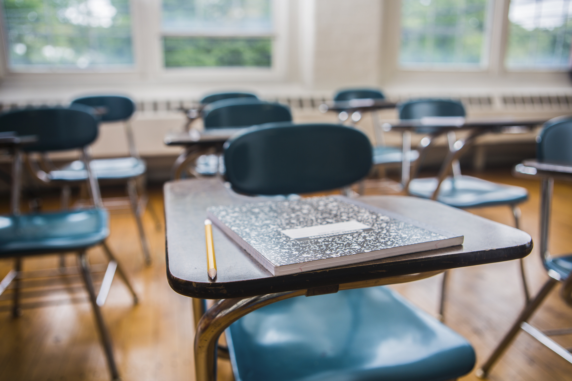 A notebook and pencil on a desk in an empty classroom waiting for kids to come back to school!